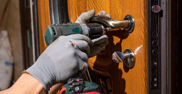 Man Installing New Door Handle And Lock Using A Drill — Locksmiths in Mermaid Beach, QLD
