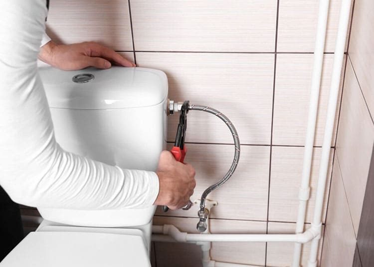 Plumber Fixing Water Hose On Toilet Cisterm — Expert Trade Services in Burleigh Heads, QLD